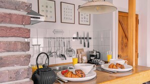 Een keuken met een bakstenen muur, een hangende kruidenrek en een houten aanrecht met ontbijtartikelen.