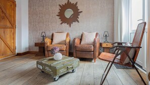 Een kamer met twee leren fauteuils, een vintage koffer, een spiegel in de vorm van een zon, en een houten deur.