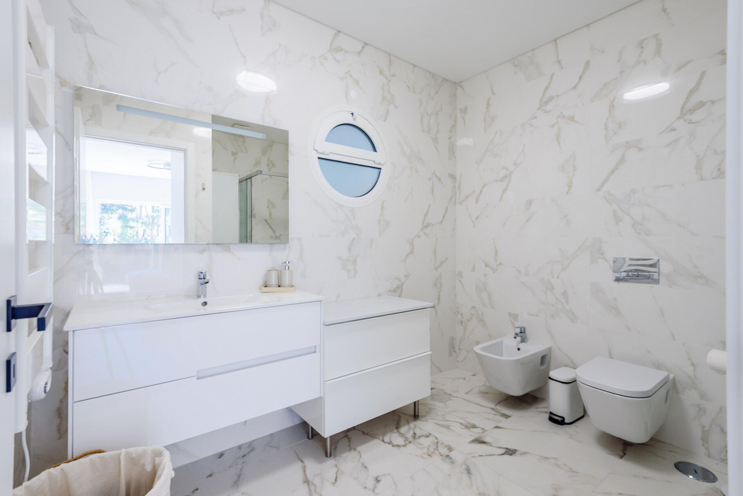Een moderne badkamer met een marmeren vloer, een witte wastafel met spiegel, een hygiëneschuiver en een toilet.