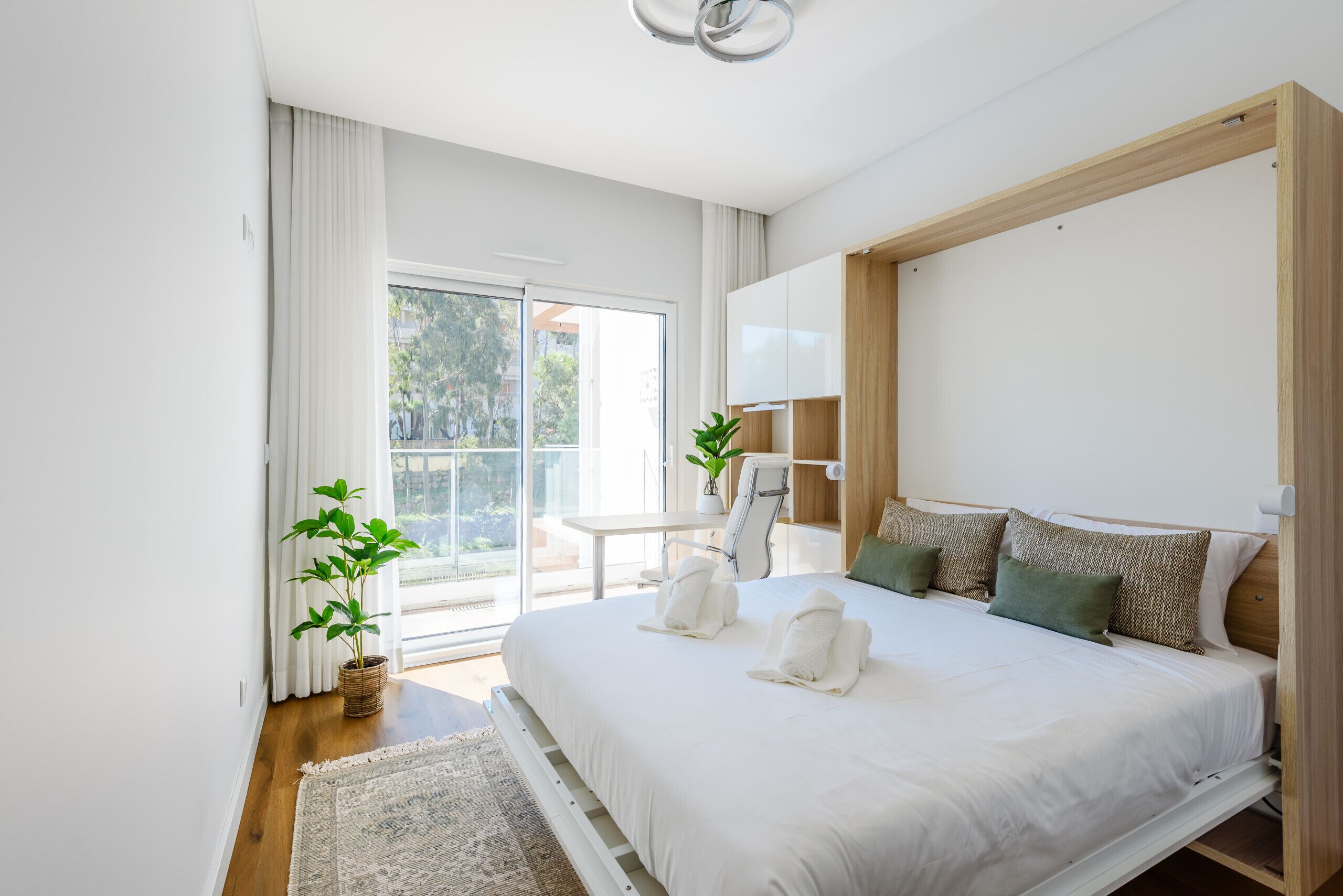 Une chambre avec un grand lit, une table de chevet, une chaise, une plante en pot et une vue sur l’extérieur grâce à une porte coulissante.