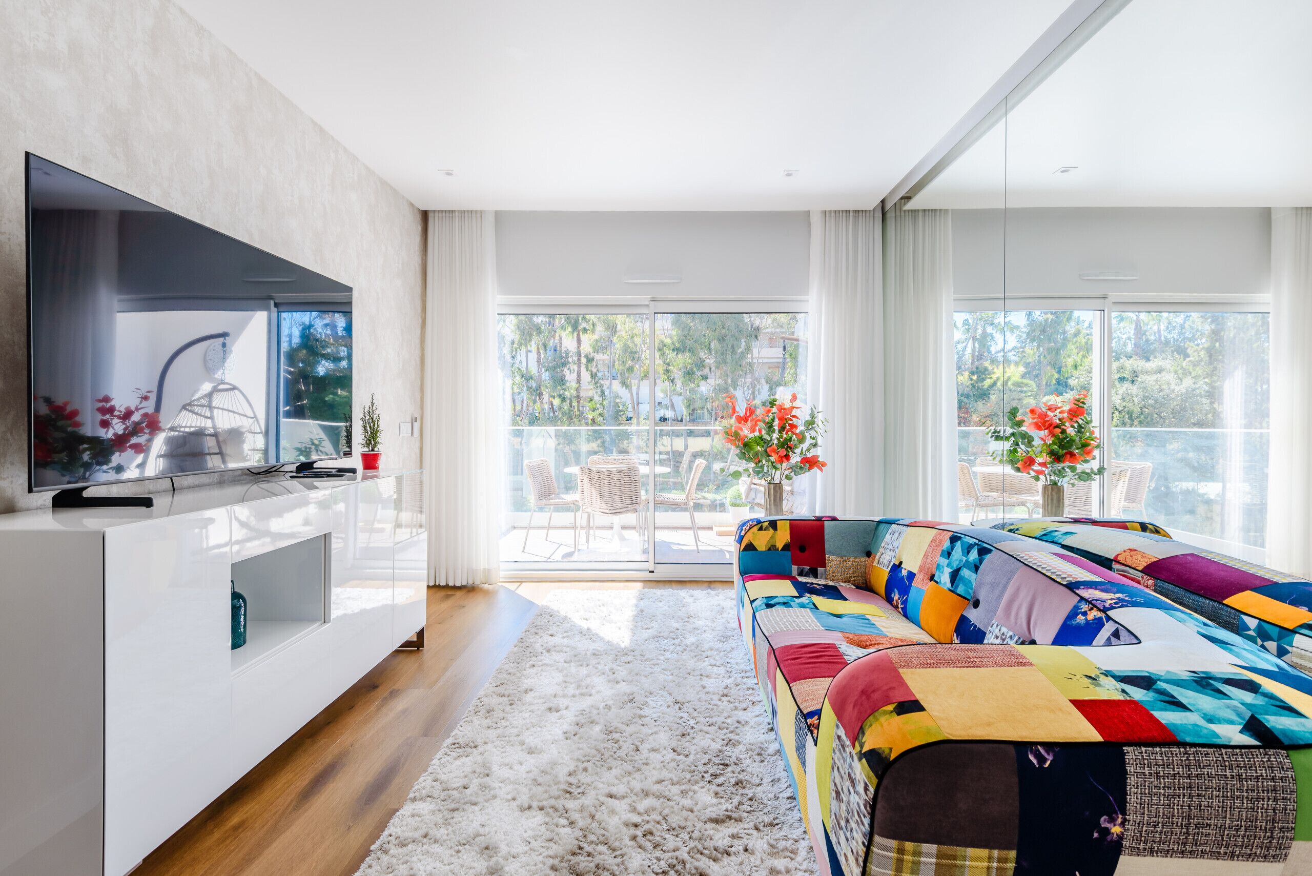 A modern living room with a large TV, a colorful sofa, and a view of the outdoors.