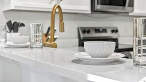 Una cocina con armarios blancos, un grifo dorado, un microondas y una estufa.