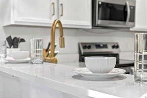 A kitchen with white cabinets, a gold faucet, a microwave, and a stove. - Magic stay near Disney (Davenport)