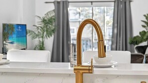 Una cocina moderna con un grifo dorado, encimera de mármol blanco y una zona de comedor con mesa y sillas blancas.