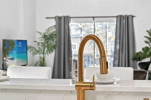 A modern kitchen with a gold faucet, white marble countertop, and a dining area with a white table and chairs. - Magic stay near Disney (Davenport)