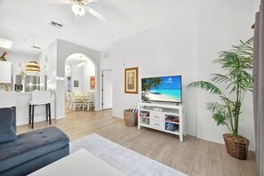 A modern living room with a flat-screen TV, a grey sofa, a dining area with white chairs, and a large potted plant. - Magic stay near Disney (Davenport)