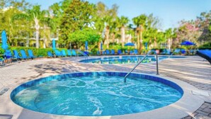 Un jacuzzi rodeado de sillones de descanso y sombrillas, con una piscina al fondo.