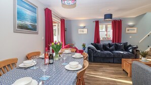 A dining area with a patterned tablecloth, chairs, and a vase of flowers. There is a sofa and a lamp in the background. - Mayfly Lodge (Bodmin)