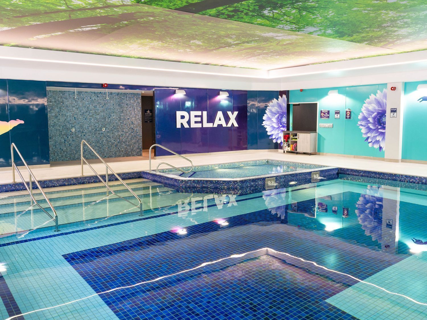 A swimming pool with a 'RELAX' sign, a tiled floor, and a wall with a floral mural.
