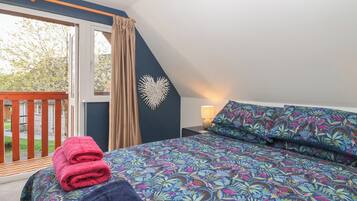 A bedroom with a large bed, a window with curtains, a wooden deck outside, and a wall-mounted decorative piece.