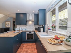 A modern kitchen with dark blue cabinets, a stainless steel range hood, a built-in oven, and a large window with a view of the outside. - Mayfly Lodge (Bodmin)