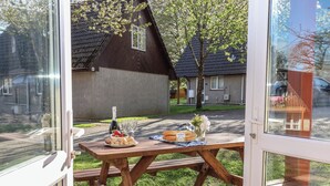 A wooden picnic table with a bottle of wine, glasses, pastries, and a vase of flowers. - Mayfly Lodge (Bodmin)