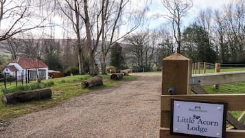 A gravel path leading to Little Acorn Lodge, surrounded by trees and a white building with a red roof.