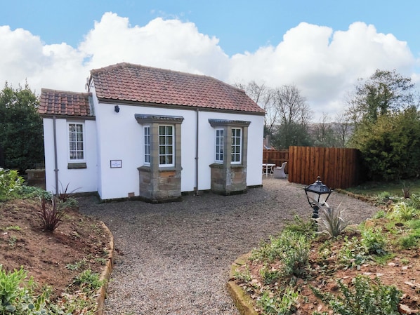 A white building with a tiled roof, stone window frames, and a gravel driveway.