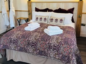 A bed with floral-patterned bedding, two folded towels, and a wooden headboard. - Little Acorn (Whitby)