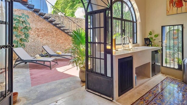 Ein geräumiger Raum mit großem Bogenfenster, einer Küchenzeile mit Spüle und einer Sitzecke mit Stuhl und Pflanze.