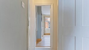 Ein Flur mit einer zur Zimmerführenden Tür, einem Lichtschalter an der Wand und einem mit Vorhängen versehenen Fenster.