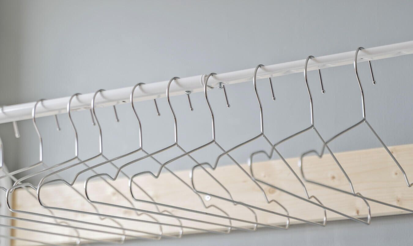 A metal drying rack with multiple hooks, mounted on a white rail, against a neutral background.