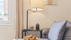 Ein Zimmer mit einer Couch, einer Lampe, einer Kaffeemaschine und einem Fenster mit Vorhängen.