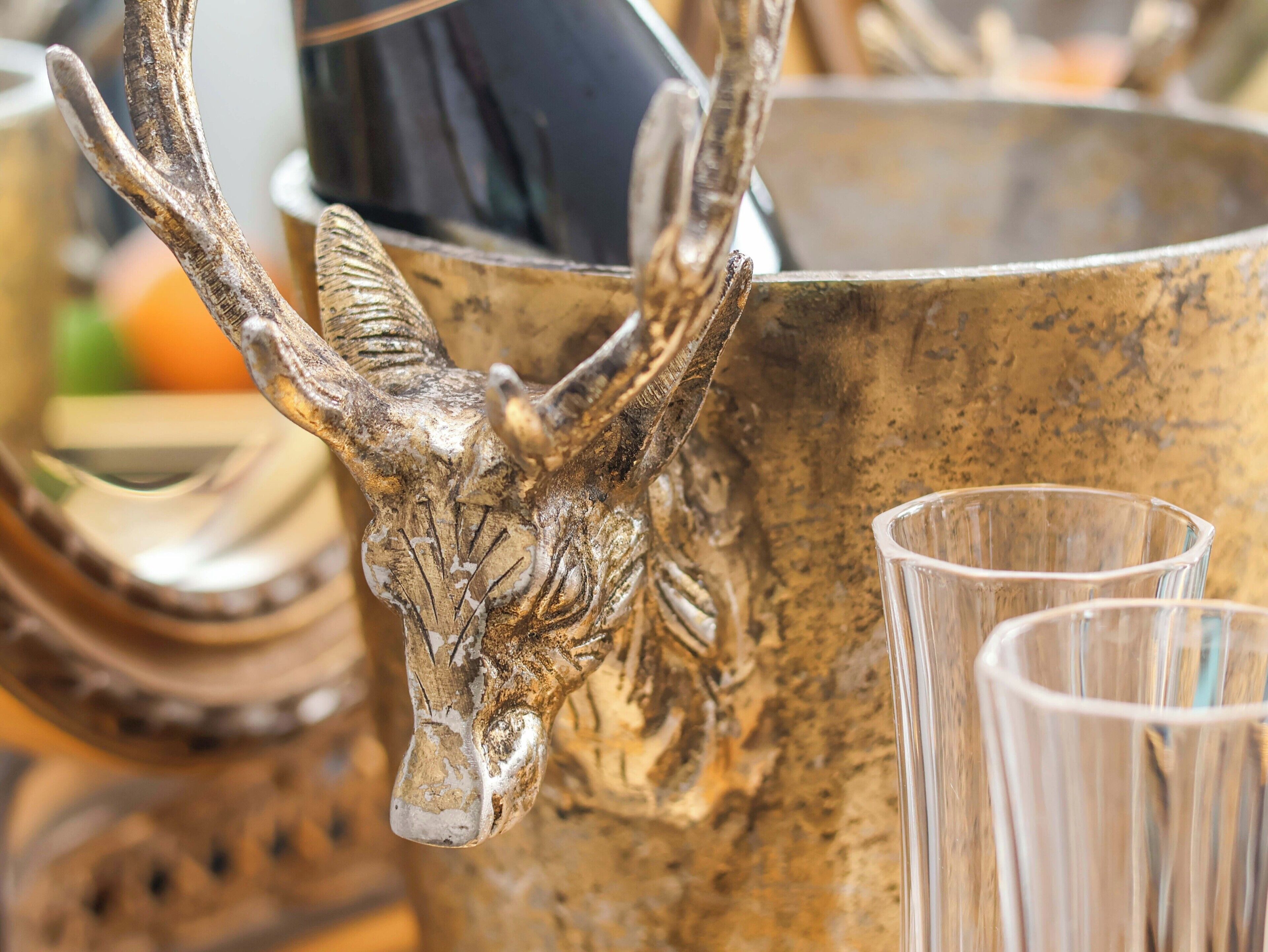 Close-up van een metalen object met een gebeeldhouwd hertenhoofd, mogelijk een decoratief item, en een glas helder water ernaast.