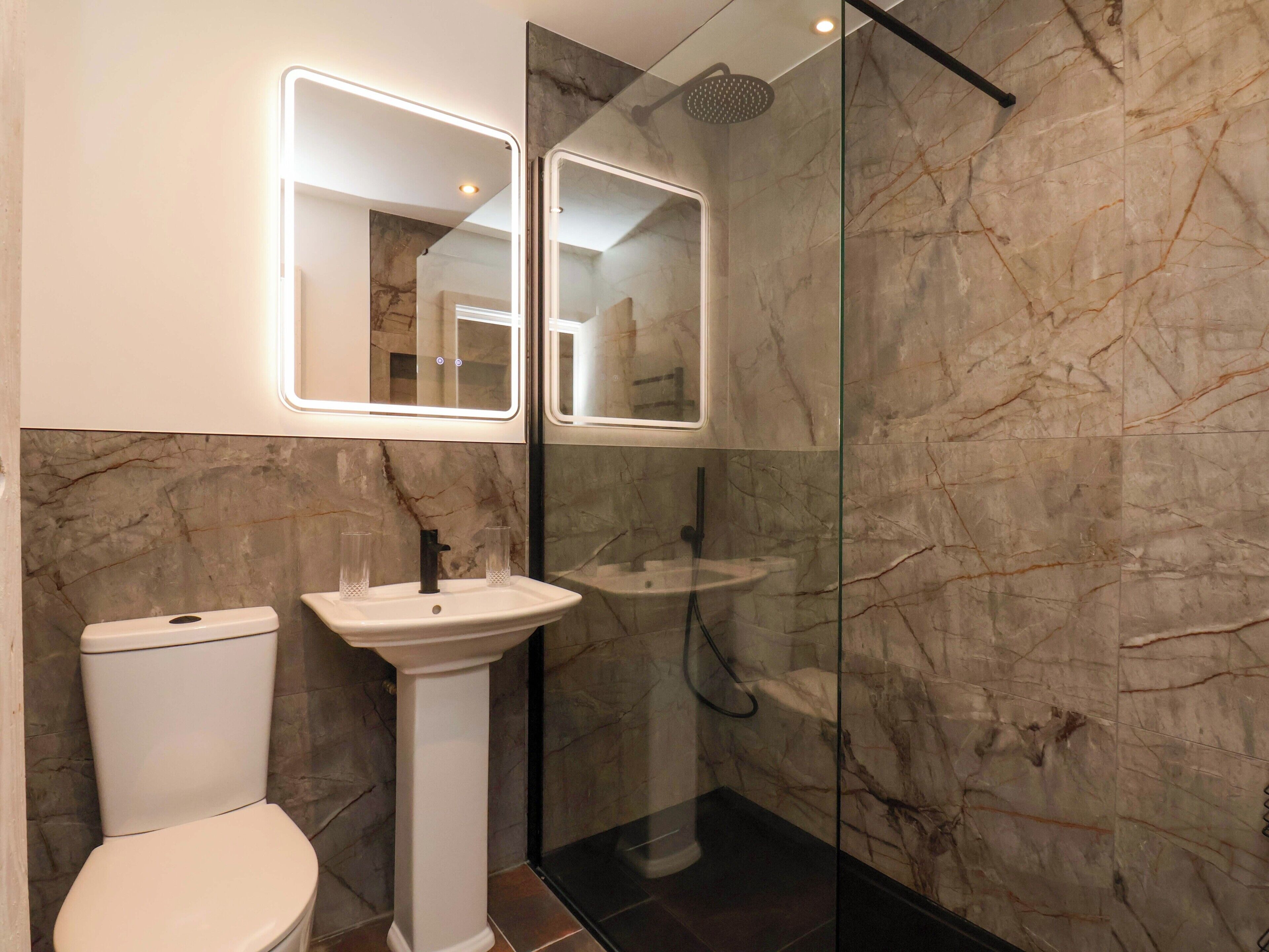 A bathroom with a toilet, pedestal sink, and a glass-enclosed shower area.