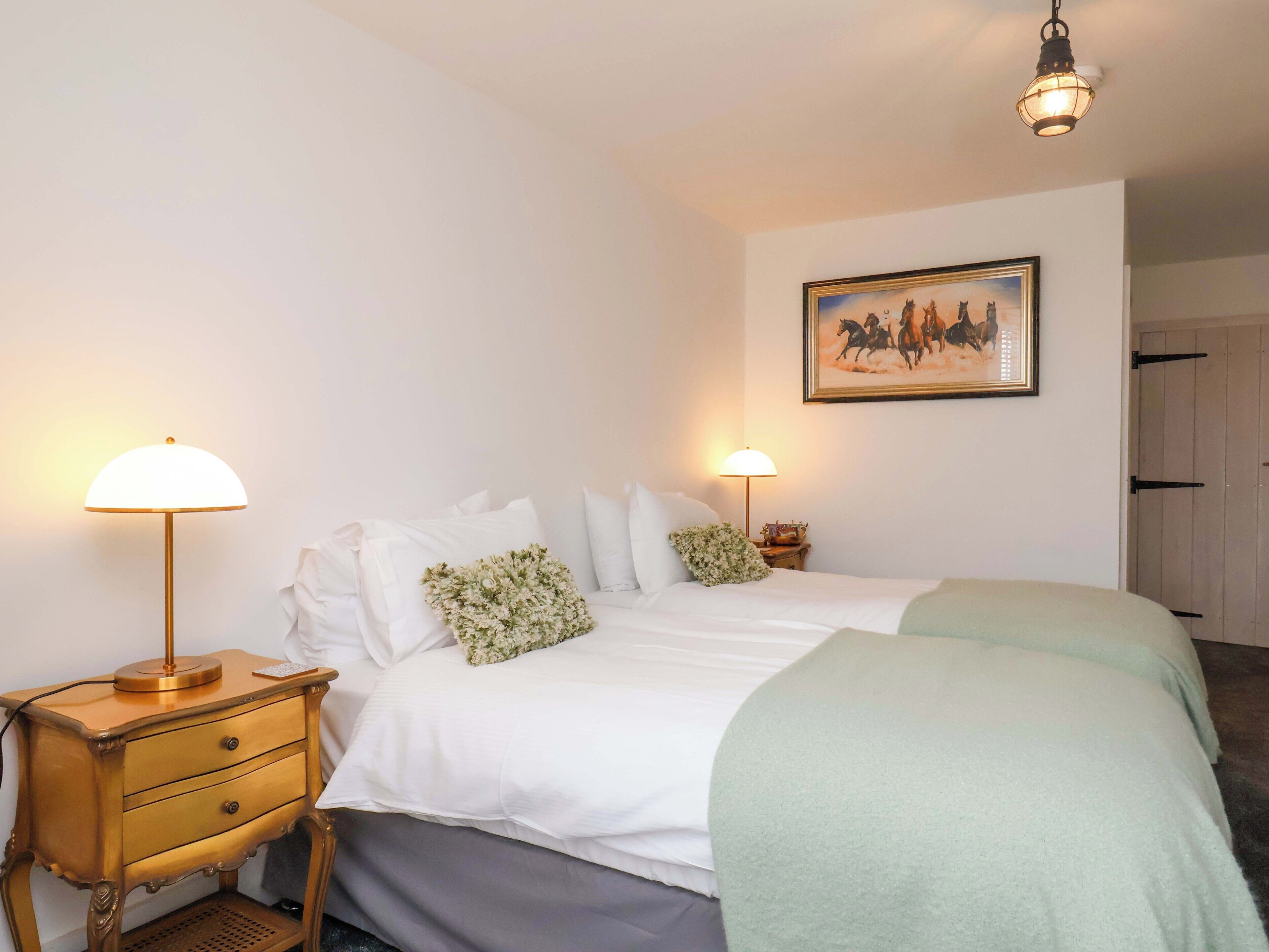 Un dormitorio con cama, mesitas de noche, lámparas, un cuadro enmarcado y una puerta.