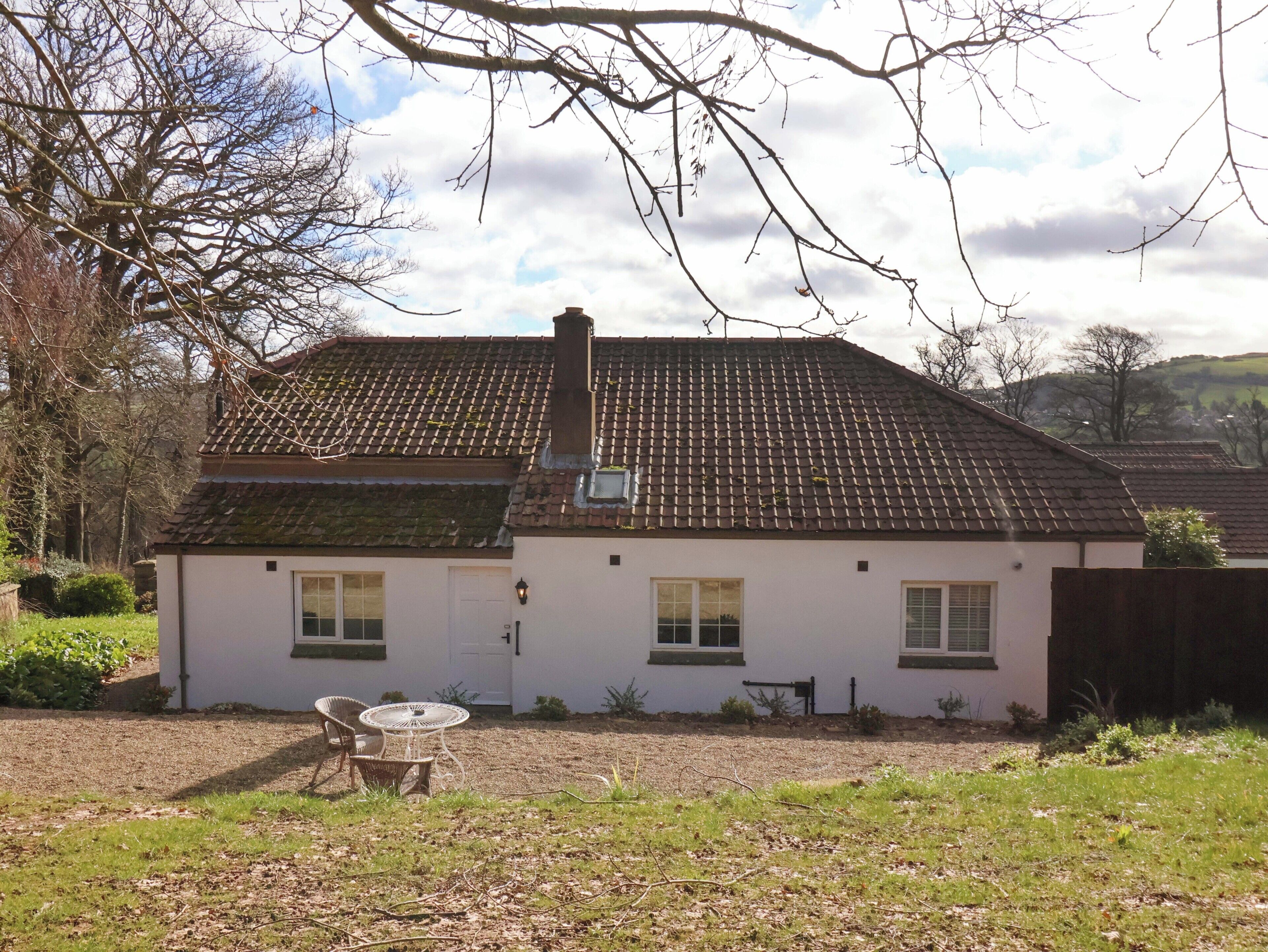 A two-story house with a tiled roof, a chimney, and a small garden with a table and chairs.