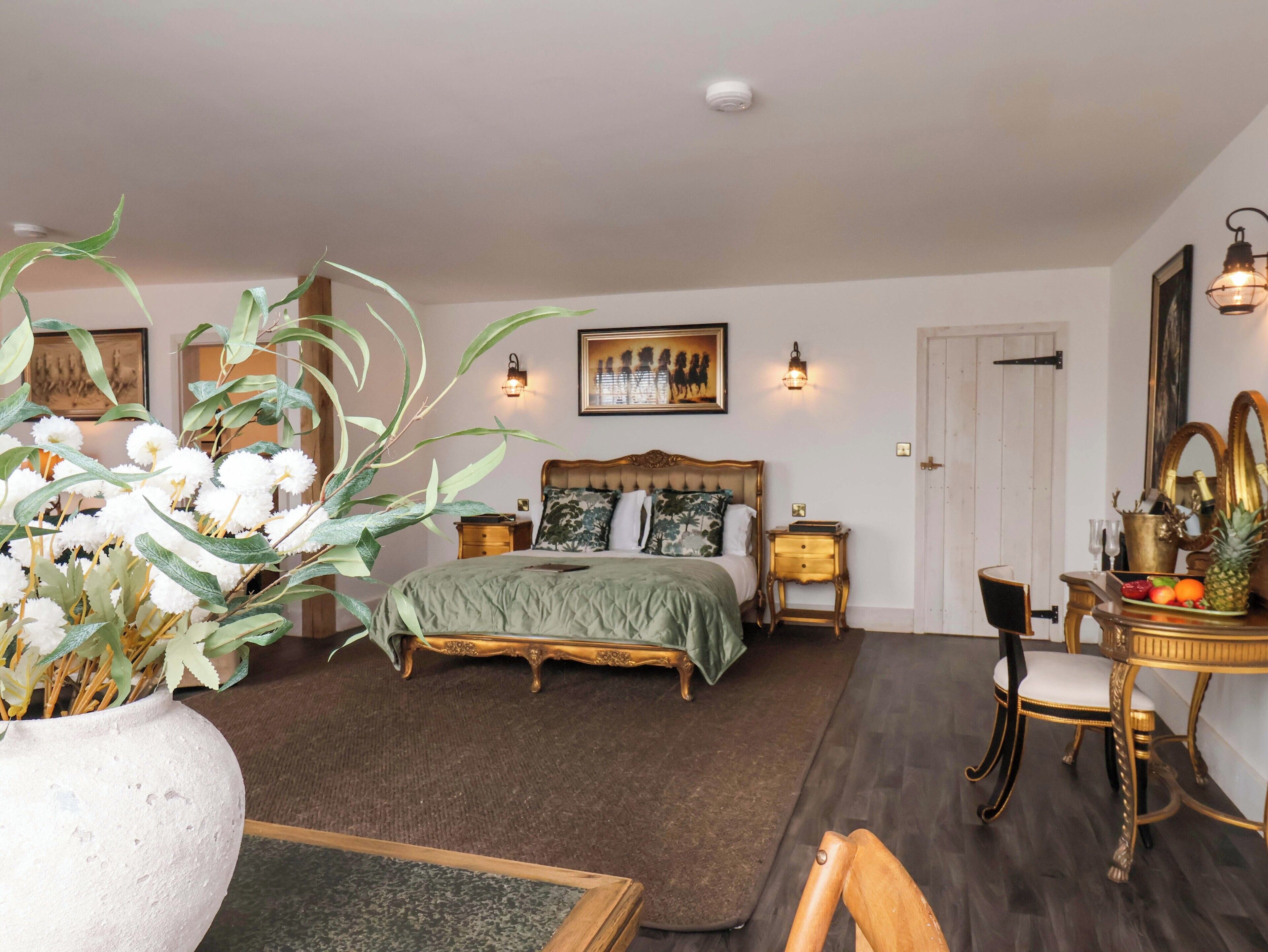 A bedroom with a bed, bedside tables, a nightstand, a chair, a dresser, a mirror, and a potted plant.