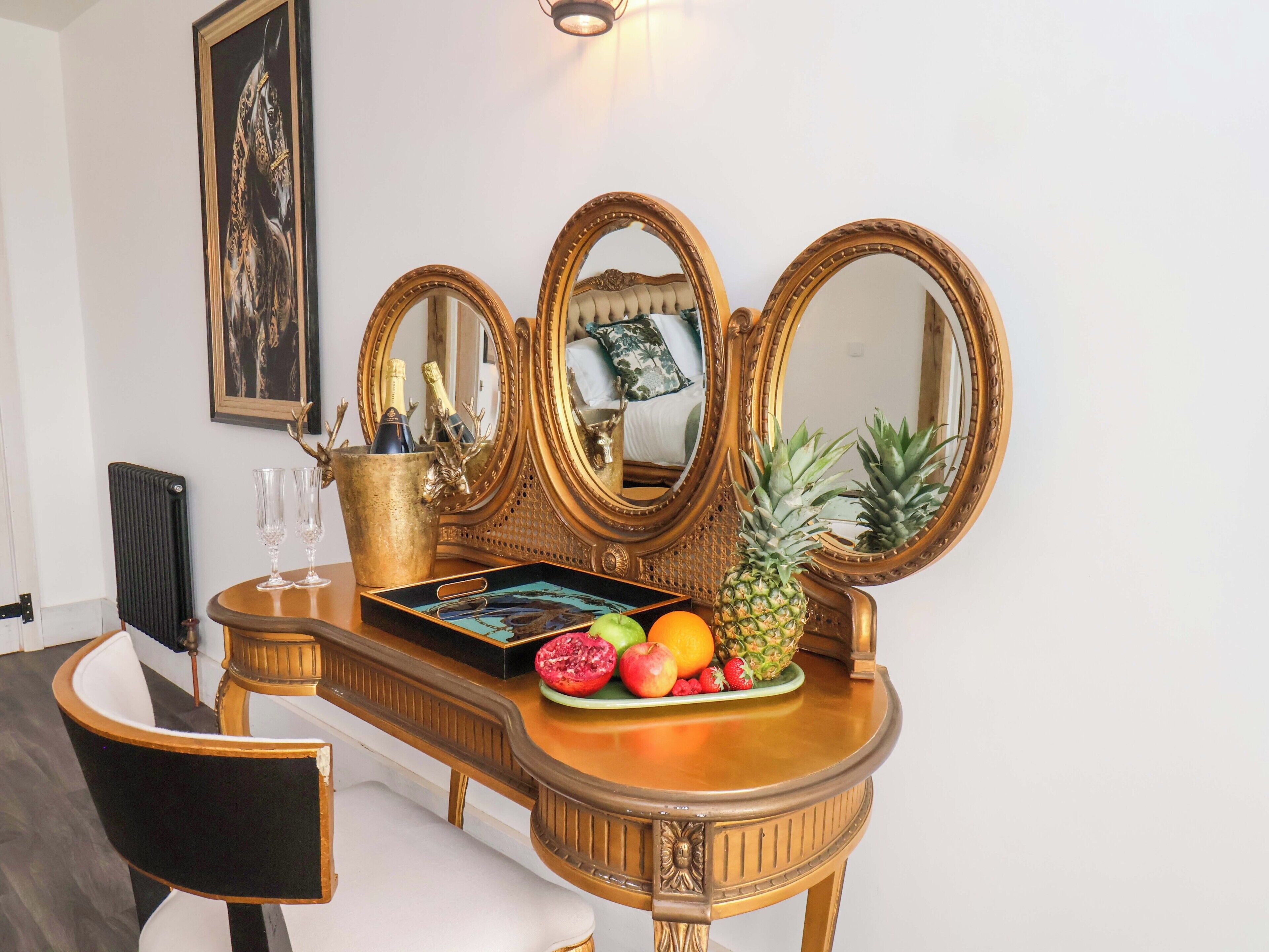A vanity with three mirrors, a fruit tray, and a bottle of champagne.