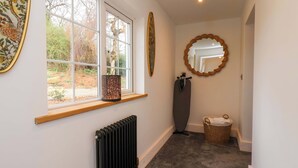 A hallway with a radiator, a window with a view of trees, a mirror, and a basket. - Hawthorn Lodge (Whitby)