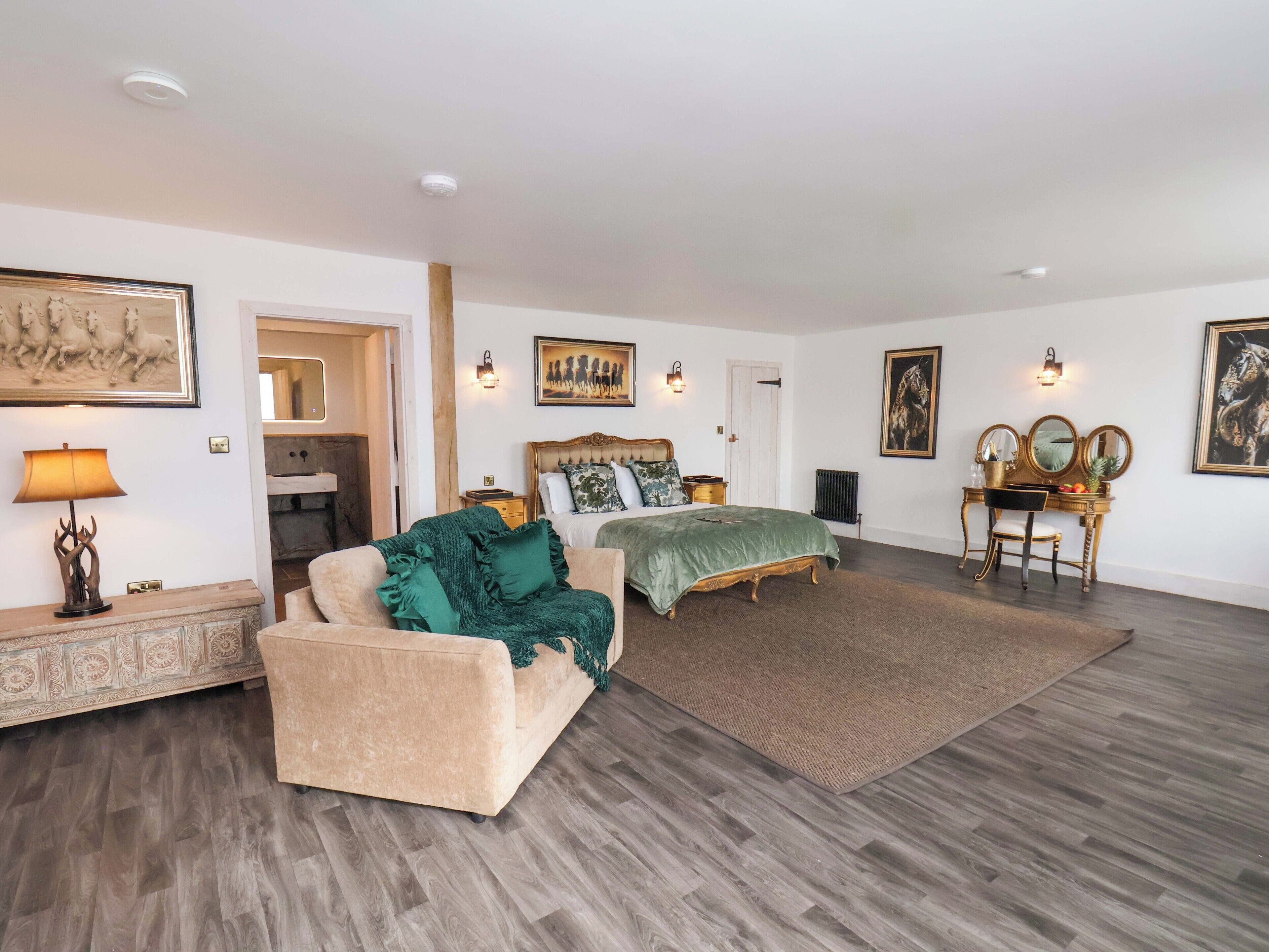 A spacious bedroom with a large bed, a sitting area with a sofa, and a vanity with mirrors.
