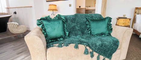 Ein beiges Sofa mit grünen Kissen und einer Decke, eine Wandskulptur eines Pferdes und eine Lampe.