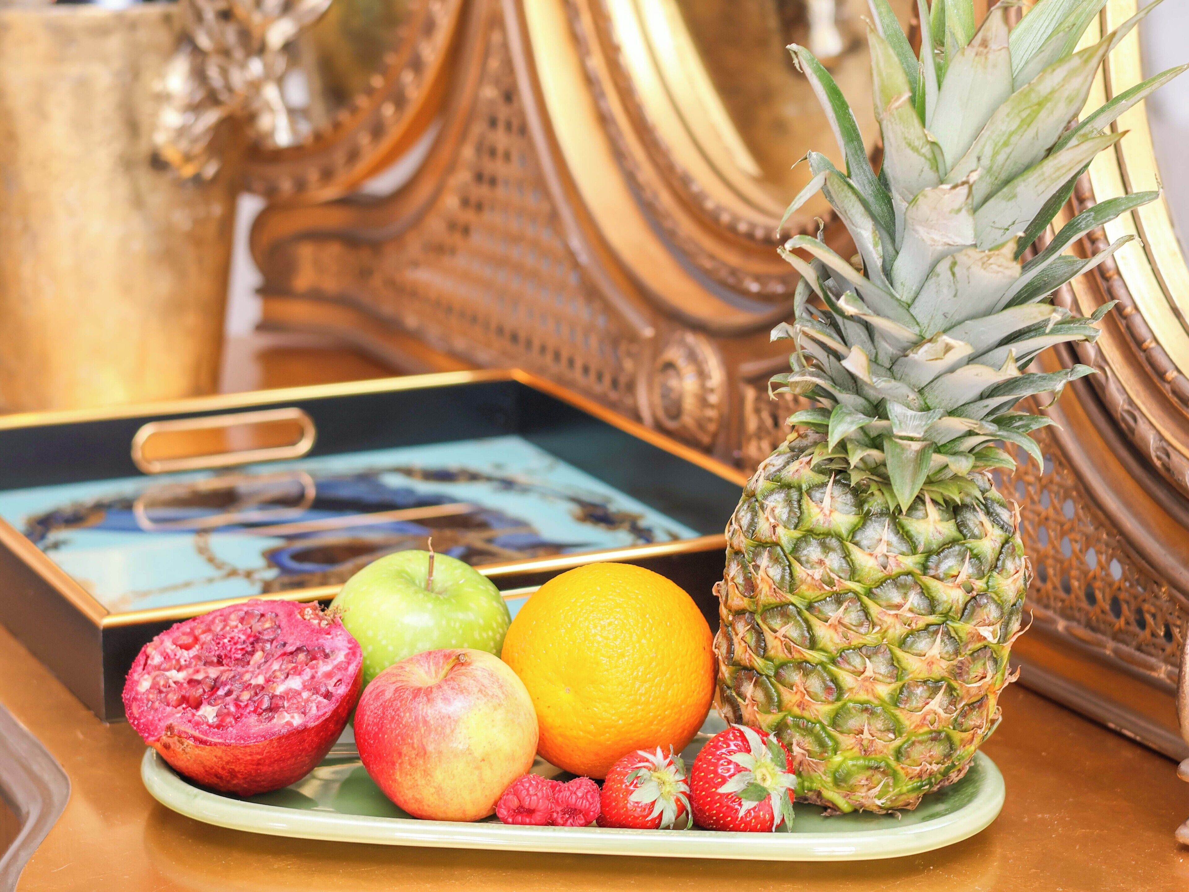 En anretning med ananas, æble, appelsin og jordbær på en tallerken.