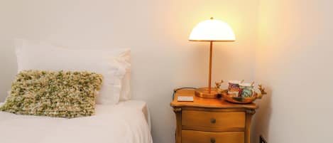 A bed with white bedding and a floral pillow, a bedside table with a lamp, and a small decorative item.