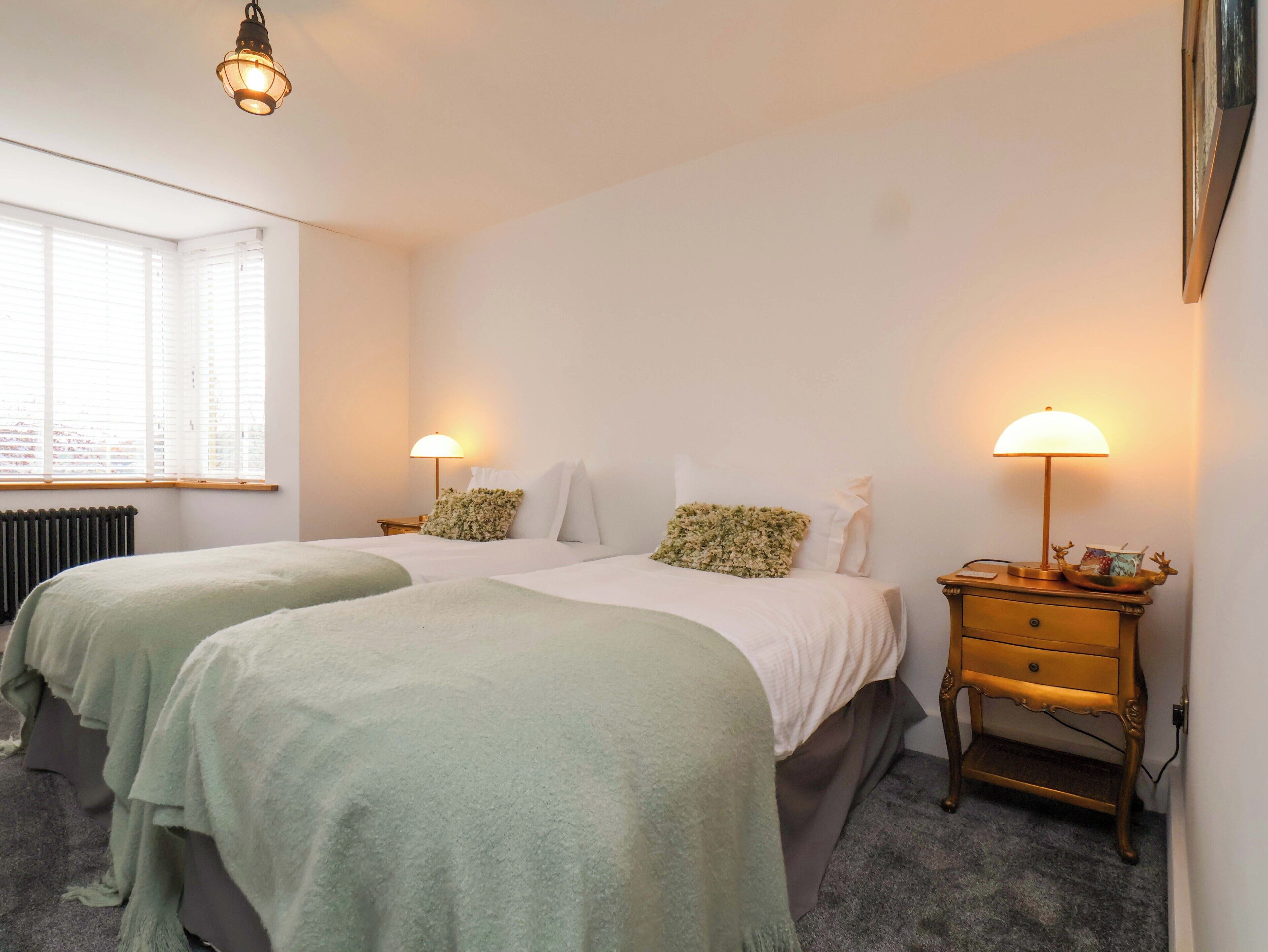 A bedroom with two beds, a nightstand, a lamp, and a radiator.