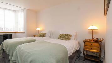 A bedroom with two beds, a nightstand, a lamp, and a radiator.