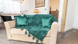 A beige sofa with green cushions and a green throw blanket, a lamp, and a framed picture on the wall. - Hawthorn Lodge (Whitby)