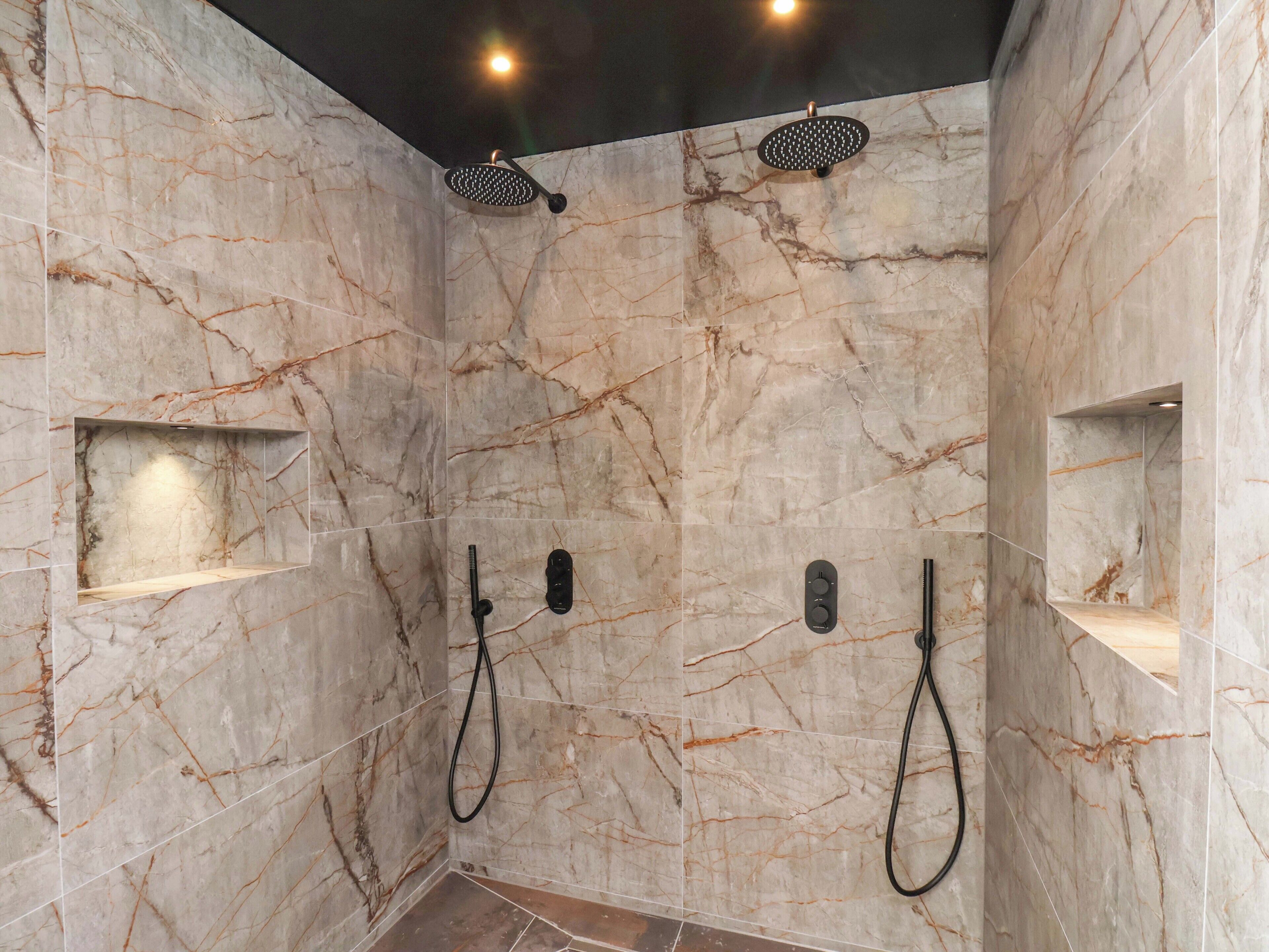 Un baño moderno con paredes de mármol, una ducha con cabezal de ducha manual y dos barras para toallas.