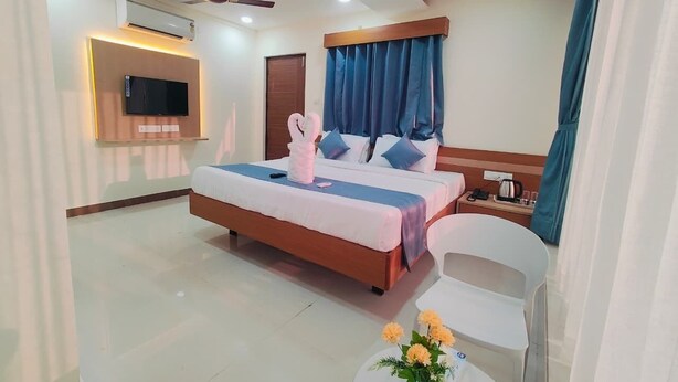 Een hotelkamer met een bed, een stoel, een tafel met bloemen, een televisie, een airconditioner en een plafondventilator.