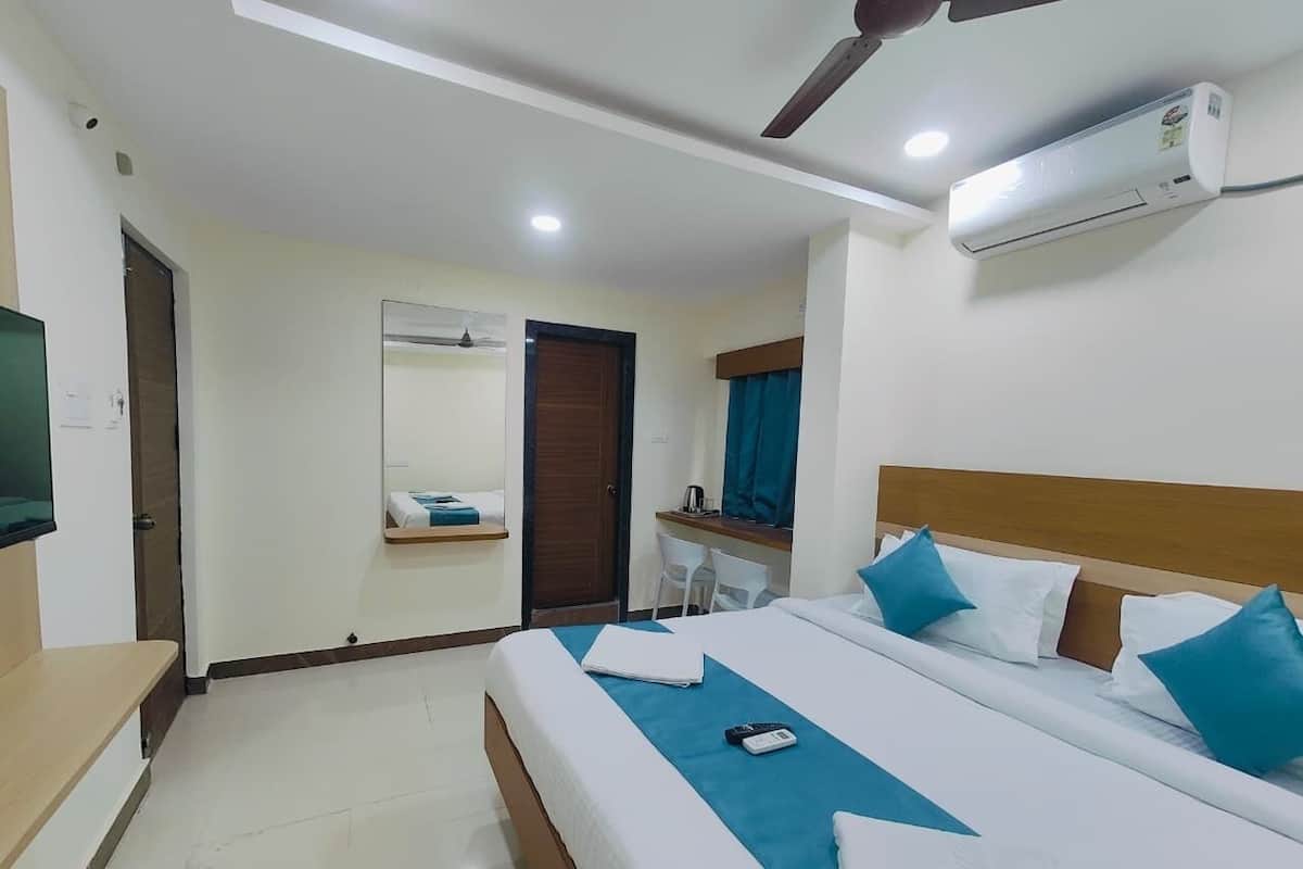 A hotel room with a bed, a desk, a chair, a TV, and an air conditioning unit.