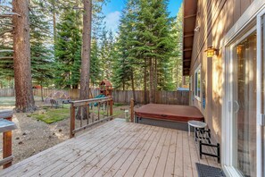Eine Holzterrasse mit Whirlpool, überdachter Sitzgruppe und Blick auf einen bewaldeten Bereich.