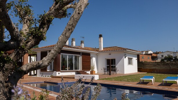 Et moderne hus med swimmingpool, terrasse med stole og udsigt over det omkringliggende landskab.