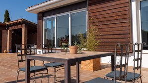 En udendørs terrasse med et bord, stole, en potteplante og en trævæg.