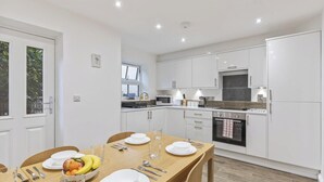 A modern kitchen with white cabinets, a dining table set with plates, utensils, and a fruit bowl. - Amy`s House - close to the Peak District! (Alton Towers & Staffordshire Villages)