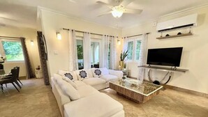Una sala de estar con un sofá modular, una mesa de centro, un televisor y un ventilador de techo.