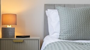 A neatly made bed with a patterned pillow and a bedside lamp on a nightstand. - Syston Townhouse With parking (Leicester)
