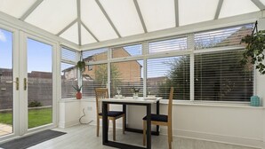 A conservatory with a table and chairs, a potted plant, and a view of the outside. - Syston Townhouse With parking (Leicester)