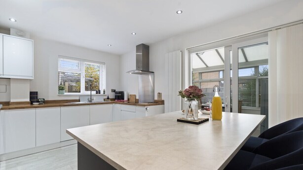 A modern kitchen with white cabinets, a large island, and a built-in stove. - Syston Townhouse With parking (Leicester)