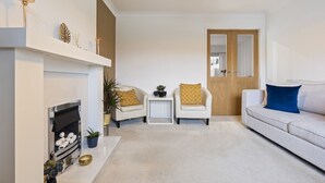 A living room with a fireplace, two armchairs, a sofa, and a small table. - Syston Townhouse With parking (Leicester)