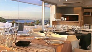 Un comedor con mesas dispuestas para una comida, ventanas amplias y vistas al mar.